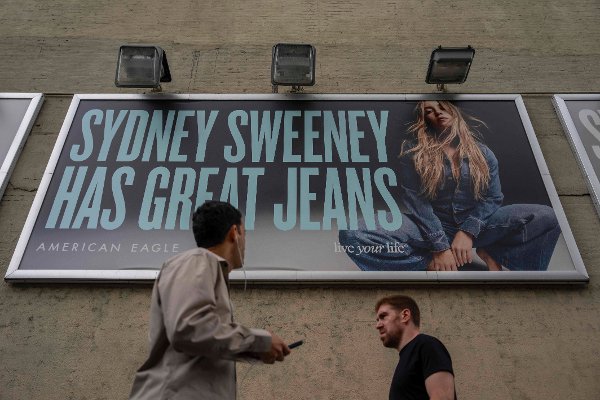 FILE - People walk past a campaign poster starring Sydney Sweeney which is displayed at the American Eagle Outfitters store, Friday, Aug. 1, 2025, in New York. (AP Photo/Yuki Iwamura, File)