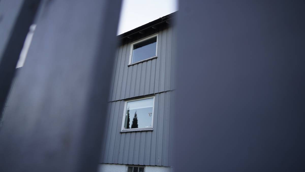 Bildet viser et grått hus sett gjennom en gjerde. To vinduer er synlige, med trær i bakgrunnen. Omgivelsene fremstår som liberale og nabolaget ser rolig ut. Lyset er dempet, trolig sent på ettermiddagen.