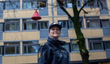 En kvinne i politiuniform står foran en gul bygning og en rød lampe.
