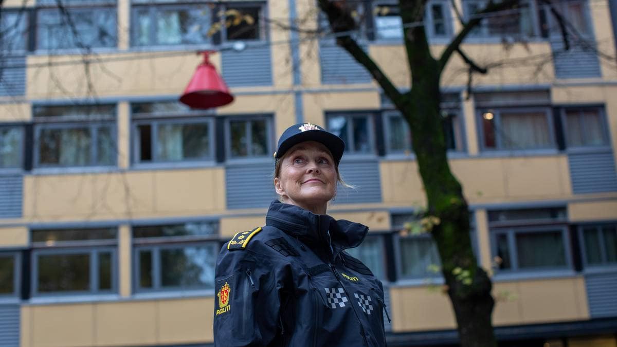 En kvinne i politiuniform står foran en gul bygning og en rød lampe.