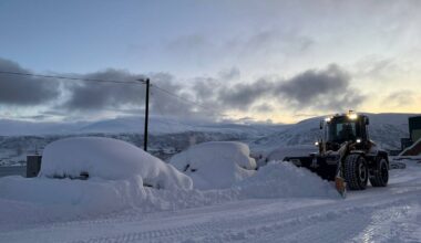 Bilene er dekt i snø i Tromsø, og en traktor brøyter ved siden av.