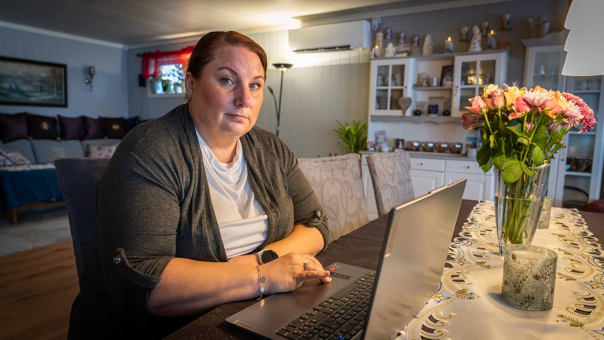 En kvinne sitter ved et bord med en laptop, iført en grå genser. Rundt henne er stoler med mønstrete trekk, og en vase med blomster står på bordet. I bakgrunnen er det en hylle med dekorative gjenstander og planter. Rommet har et varmt og koselig preg med naturlig lys.