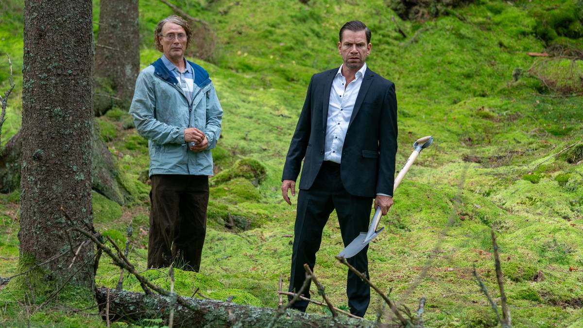 To menn står i skogen. Den ene har en spade i hånden.