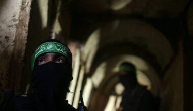 To personer iført militære klær står i en mørk, smal gang. Den ene har et hodesett og ser fremover, mens den andre står i bakgrunnen. Omgivelsene er preget av murvegger og lite lys. Bildekonteksten antyder en sikkerhetsoperasjon.