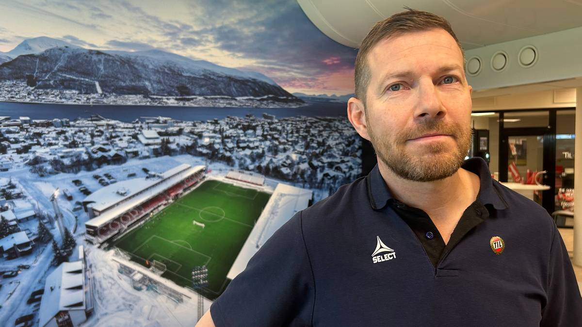 En mann står i et rom med en stor veggmaleri av et vinterbilde av en fotballstadion og omkringliggende områder. Han har på seg en t-skjorte med klubbemblem og en jakke med logo. Omgivelsene inkluderer stoler rundt et bord, samt sportsutstyr synlig i bakgrunnen. Rommet har moderne innredning og godt lys. (Bildebeskrivelsen er laget av en KI-tjeneste)