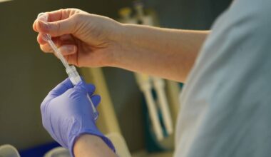 En person iført hansker holder en pipette over et prøveglass. Hendene er fokuspunktet, med tydelig aktivitet knyttet til prøvetaking. Omgivelsene er laboratoriemessige, med pipetter og beholdere synlig i bakgrunnen. Bildet illustrerer et typisk arbeidsmoment i laboratorieforskning. (Bildebeskrivelsen er laget av en KI-tjeneste)