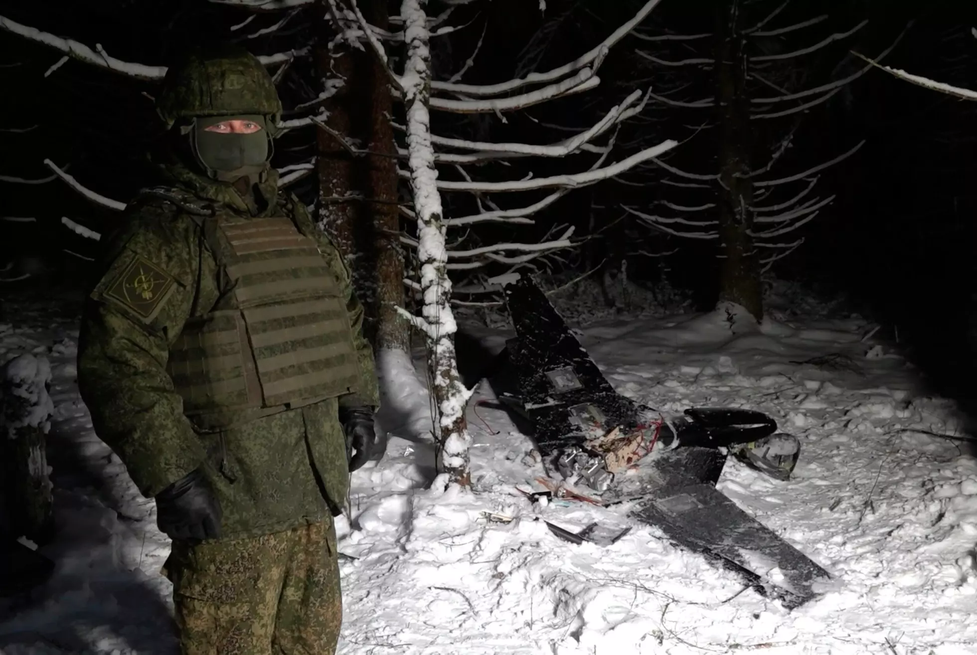 PÅSTÅR DET ER BEVIS: En soldat viser fram det Kreml hevder er en drone brukt av ukrainerne til å angripe Putins residens, avbildet i et bekmørkt, flombelyst skogholt i snøen. Uavhengige medier og researchere har ikke funnet spor etter det angivelige angrepet, som man vanligvis gjør etter ukrainske droneangrep i Russland. Pensjonert generalløytnant Arne Bård Dalhaug har ingen tro på at bevisene er ekte. Foto: Russlands forsvarsdepartement