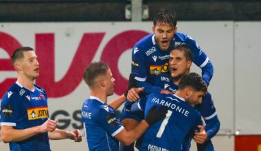 Fotballspillere i blå drakter går av banen etter en kamp, omgitt av tåke. I forgrunnen går en spilleder i gul drakt. Det er svakt opplyst av stadionlys i bakgrunnen. Stemningen er urolig, muligens på grunn av hendelser under kampen.