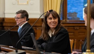 Tre advokater i sorte kapper sitter ved en dommerbenk i en rettssal.