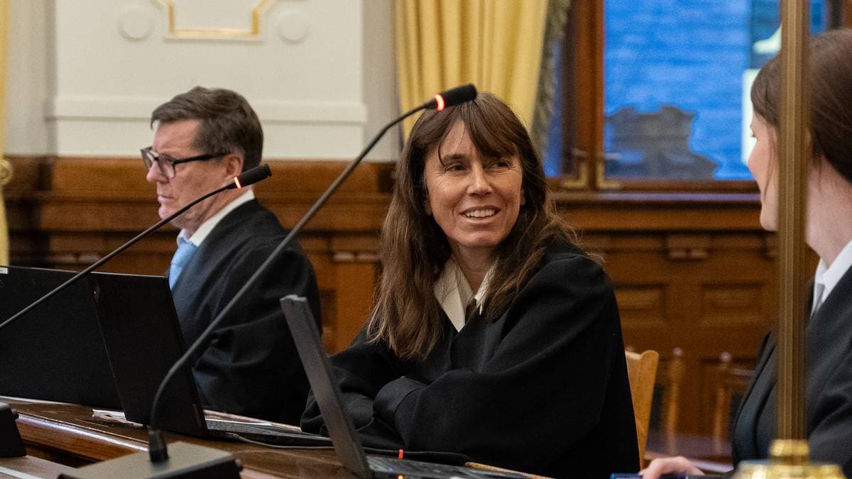 Tre advokater i sorte kapper sitter ved en dommerbenk i en rettssal.