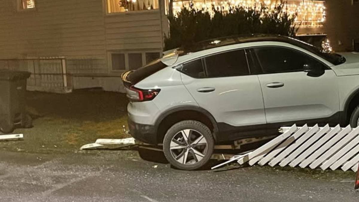 Et grått SUV kjøretøy står på en vei foran en bolig med vinduer lysende i natten. En del av et gjerde ligger på bakken ved siden av bilen, som antyder at det har vært en kollisjon. Boligen har julelys hengende, og det er mørkt i omgivelsene. Ingen personer er synlige i bildet. (Bildebeskrivelsen er laget av en KI-tjeneste)