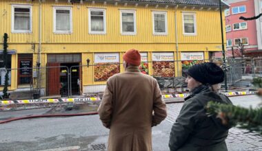 et par personer som går forbi en gul bygning (Bildebeskrivelsen er laget av en KI-tjeneste)