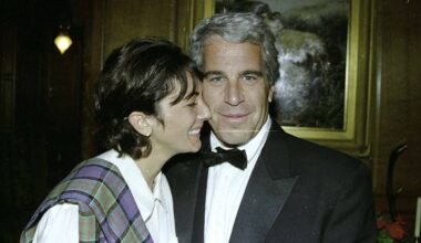 To personer står sammen i en formell setting iført dress og tartansjal. Bildet viser en dekorativ innrammet maleri og trepanel i bakgrunnen. Scenen er lys med en lykt i bakgrunnen som kaster et mykt lys. En etikett i nederste hjørne merket "GOVERNMENT EXHIBIT 321" indikerer bildet som bevis i en sak. (Bildebeskrivelsen er laget av en KI-tjeneste)