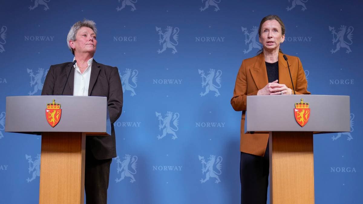 To personer står bak hver sin talerstol med mikrofon under en pressekonferanse i Norge. Bakgrunnen er dekorert med riksvåpenet til Norge og teksten "NORWAY". Talerstolene har embetssegl preget på fremsiden. (Bildebeskrivelsen er laget av en KI-tjeneste)