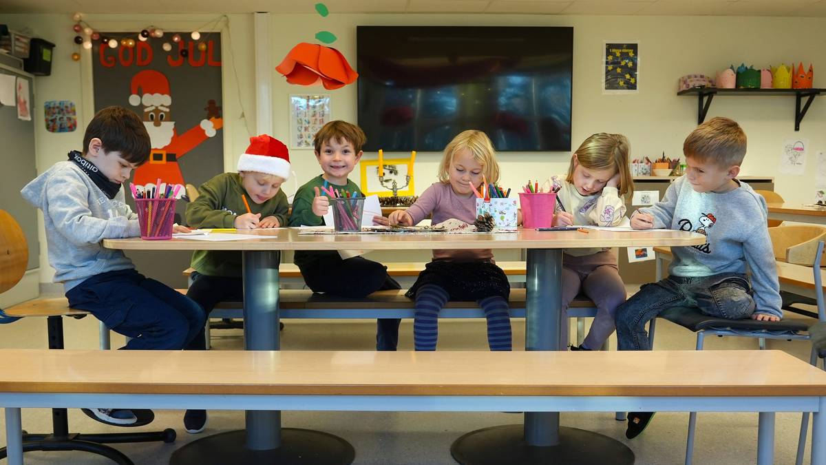 En gruppe barn sitter og tegner ved et langbord. En av dem har på en nisselue og klasserommet er dekorert med julepynt.