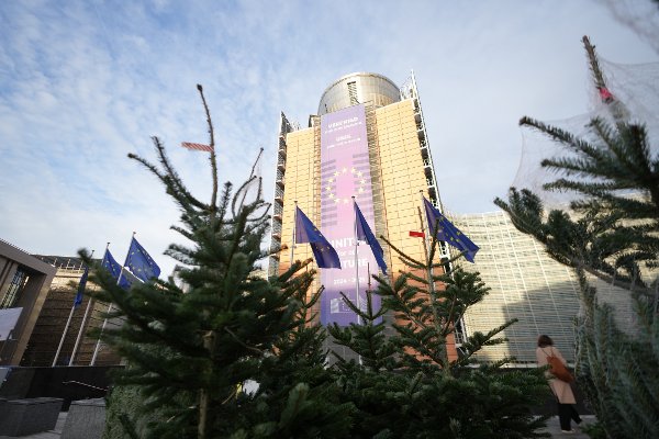 A woman walks past holiday trees for sale outside the European Commission headquarters in Brussels, Tuesday, Dec. 9, 2025. (AP Photo/Virginia Mayo)