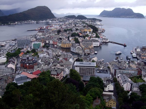 Ålesund 20140801 Ålesund by sett fra Fjellstua på byfjellet Aksla. 
Det var ikke mye igjen av Ålesund etter brannen i 1904, men takket være byggekrakk i resten av landet, strømmet bygningsarbeidere til fra hele Norge. Byen ble gjenoppbygd på rekordtid, og i den enhetlige Jugendstilen som er blitt Ålesunds varemerke. 
Ett brudd i det ellers ganske enhetlige bybildet er Rådhuset tv. i bildet, bygget på tomten til den bortsprengte Rønneberghaugen. Hovedarkitekt var Sverke Mogstad, og bygget sto ferdig i 1980. I 2012 fikk rådhuset ny fasade i glass og aluminium, og er muligens ikke lenger Norges nest styggeste bygg, slik det fremsto i en kåring få år tidligere. 
Byparken i forgrunnen er overgrodd, men man skimter nede th Keiser Wilhelm II monumentet som ble reist i 1910, bl.a. for hans innsats for brannofrene i 1904. 
Foto: Marit Rasmussen / NTB
((Sammenholdes med Mary Evans foto nr sz9511d9 fra ca 1890 i NTB basen)
