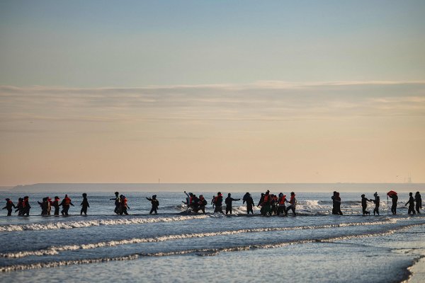 (FILES) Migrants wade into the sea to try to board smugglers' boats in an attempt to cross the English Channel off the beach of Gravelines, northern France on September 27, 2025. Prison sentences ranging from one to nine years were requested on December 9, 2025 against 17 suspected smugglers on trial since December 1 in Lille, accused of using 