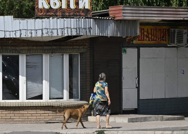 A dog and a woman walk past closed shops in a street of the town of Myrnohrad on August 26, 2024, amid the Russian invasion of Ukraine. (Photo by Genya SAVILOV / AFP)