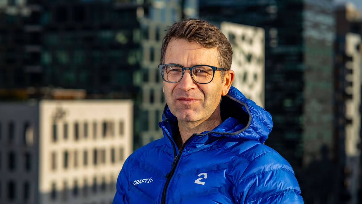 En person iført en blå jakke med logoene til TV 2 og Craft står foran høyhus i urbane omgivelser. Bakgrunnen viser moderne arkitektur med høye bygninger. Bildet er tatt i dagslys, noe som gir skarp belysning. (Bildebeskrivelsen er laget av en KI-tjeneste)