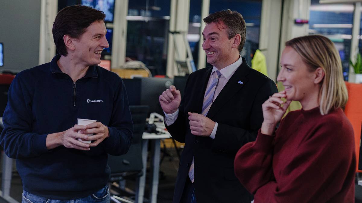 Tre personer står i et kontorlandskap og diskuterer. En av dem holder en pappkop, mens de andre gestikulerer. Det er datamaskiner og kontormøbler i bakgrunnen. Atmosfæren virker uformell. (Bildebeskrivelsen er laget av en KI-tjeneste)