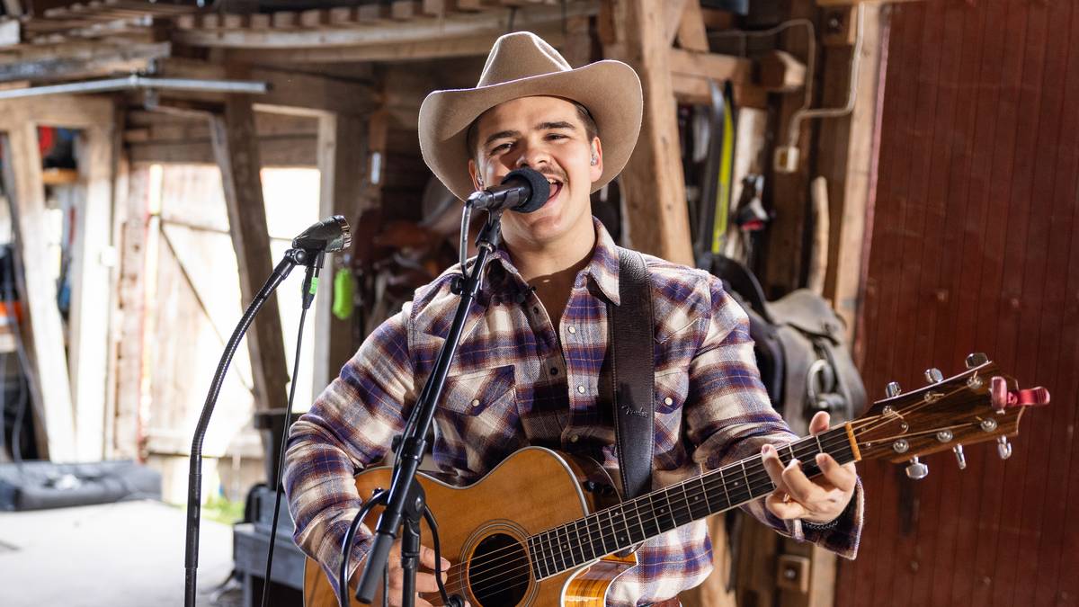 Tobias Sten spiller gitar og synger i mikrofonen. Har på seg en rutete skjorte, cowboyhatt og skjorta ned i buksa.