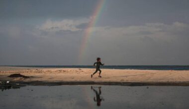 En barnløp på stranden under en regnbue, med havet i bakgrunnen.