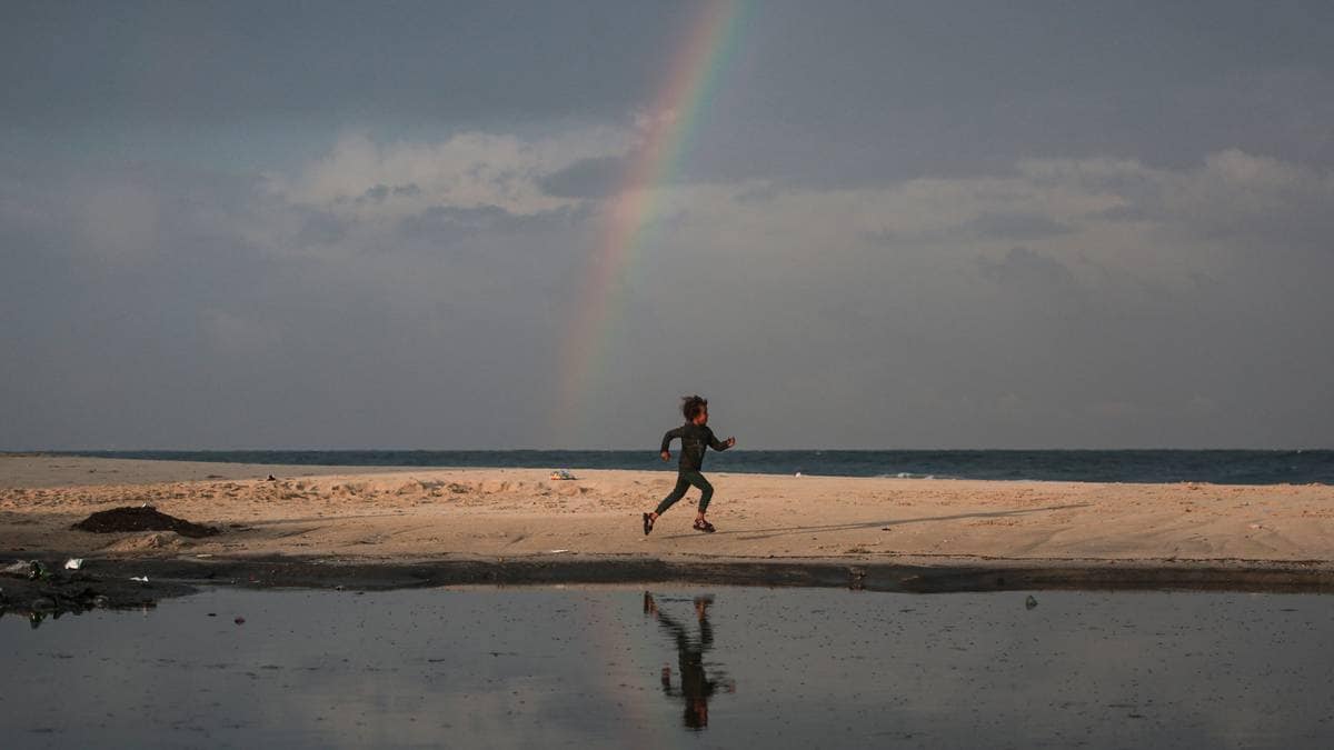 En barnløp på stranden under en regnbue, med havet i bakgrunnen.