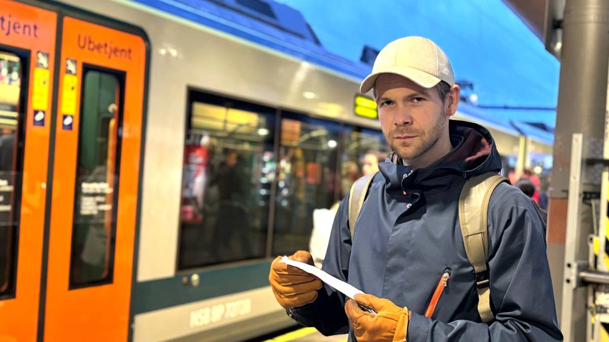 En mann står på en perrong foran et tog. Han har en kvittering i hånda. Han har på seg lue og jakke, og sekk.