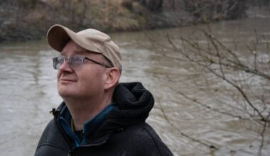 en person med hatt og briller ved en elv