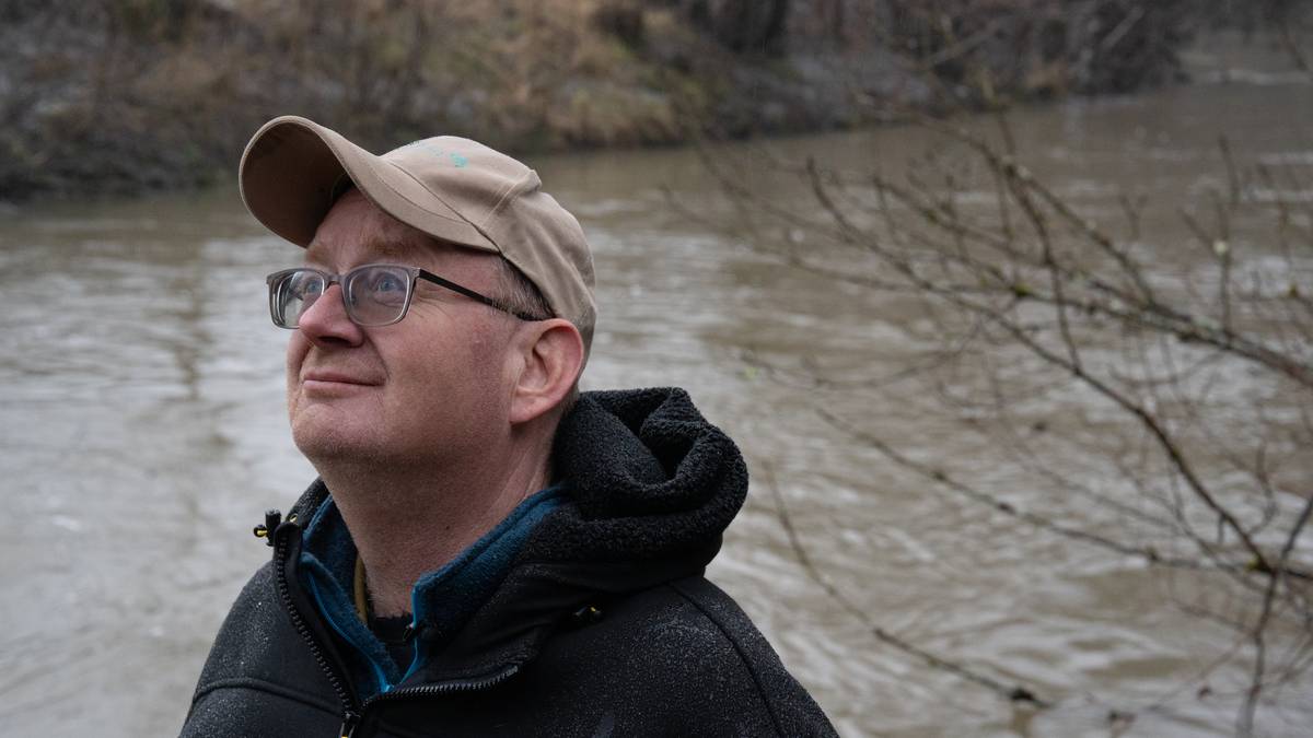 en person med hatt og briller ved en elv