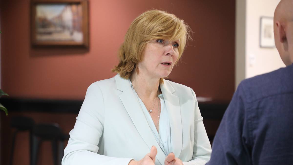 En person i lys dress gestikulerer mens de snakker med en annen person i mørk blå jakke. Omgivelsene inkluderer en vegg med maleri i bakgrunnen. Deler av rommet ser ut til å være et møteområde. (Bildebeskrivelsen er laget av en KI-tjeneste)