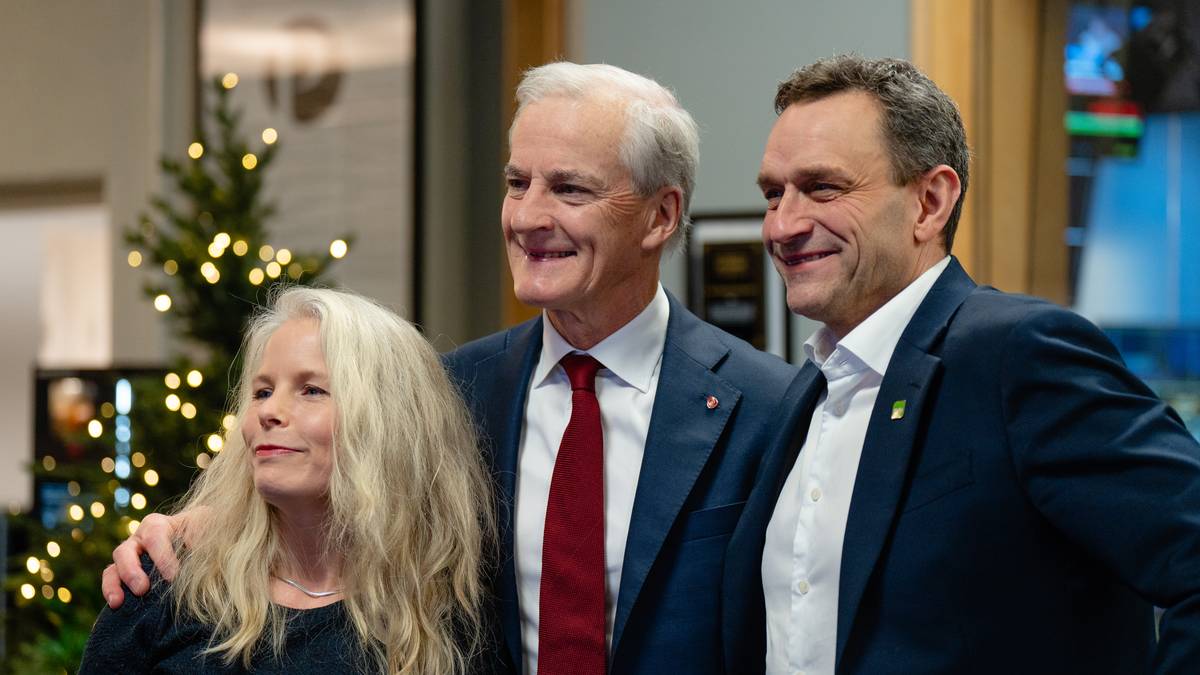 Tre personer står sammen foran et industrielt bakteppe. To av dem er kledd i mørke dresser, mens den ene har på seg en svart topp. Det er en juletre med lys i bakgrunnen, som gir en festlig stemning. Alle smiler mot kamera.