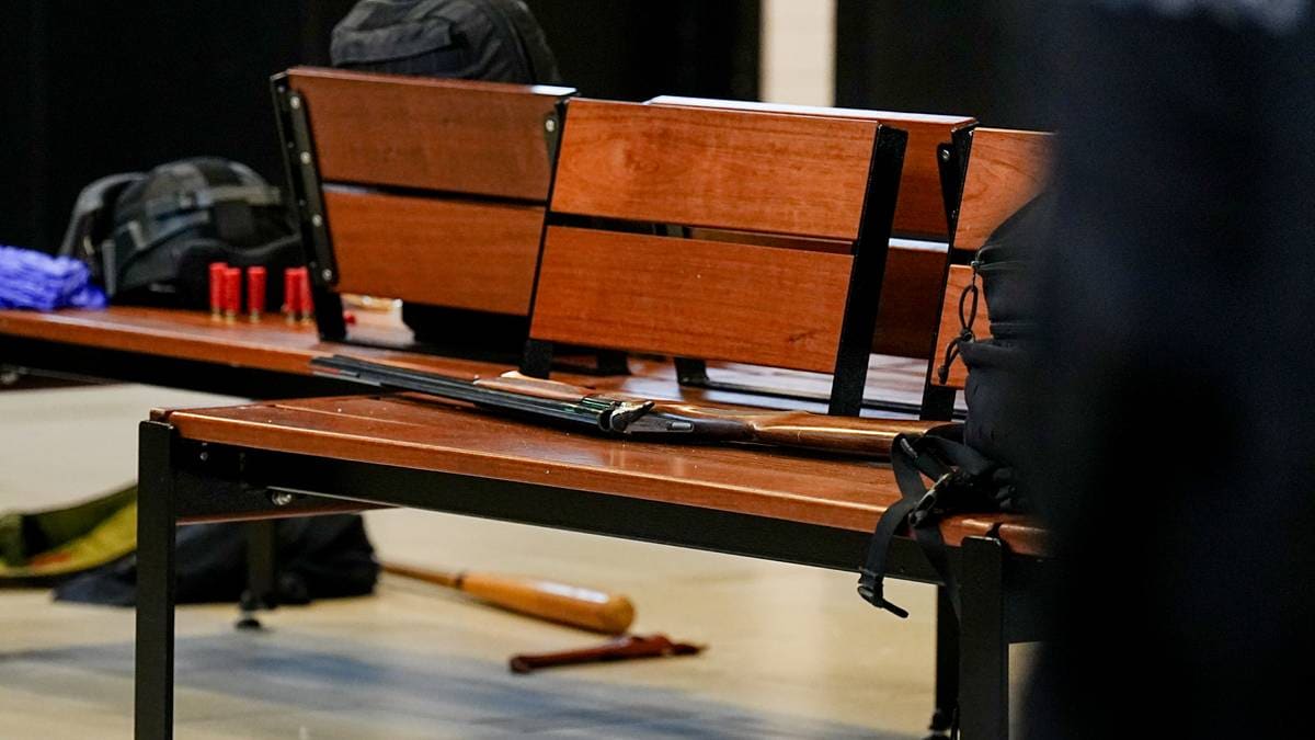 En benk i en offentlig bygning viser ulike eiendeler, inkludert en rifle, utstyr og ryggsekker. Det er også en baseballkølle i forgrunnen. Omgivelsene har et moderne interiør med fliser på gulvet og en dør i bakgrunnen. Ingen personer er synlige i bildet. (Bildebeskrivelsen er laget av en KI-tjeneste)