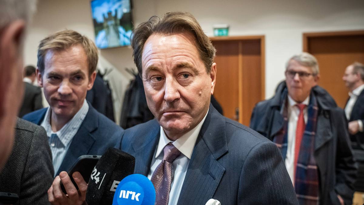 Flere personer deltar i en pressekonferanse. En mann i dress snakker med journalister som holder mikrofoner. Omgivelsene har en enkel innredning med en skjerm i bakgrunnen. Andre personer står i bakgrunnen og observerer situasjonen. (Bildebeskrivelsen er laget av en KI-tjeneste)