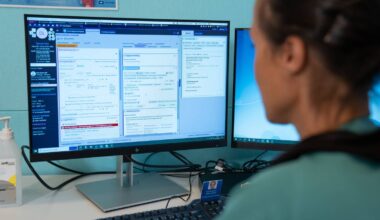 Rachel DilleAmdam sitter vendt mot en dobbel dataskjerm. På skjermen ser man litt av hvordan Helseplattformen ser ut. DilleAmdam er ufokusert i bildet.