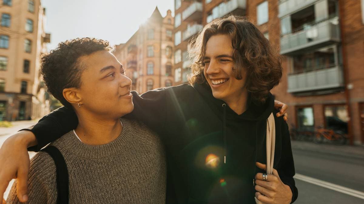 En smilende ung mann holder armen rundt en kamerat i en bygate.