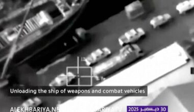 Et skip blir lastet av med våpen og militære kjøretøy i en havn.