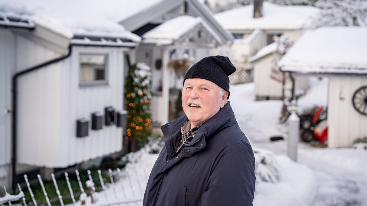 En eldre mann står foran snødekte hus i en boliggate. Han har på seg en mørk jakke og en lue. Bak ham er det julelys på et tre og flere postkasser. Omgivelsene er rolig med snø på bakken og hus i bakgrunnen.