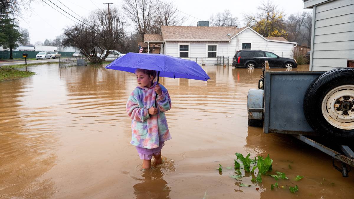 Bildet viser en liten jente med en lilla paraply. Hun står i regnvann opp til leggene utenfor hjemmet sitt i California.