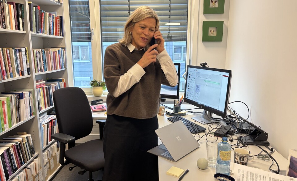 Kvinne står foran skrivepult med PC og snakker i telefonen