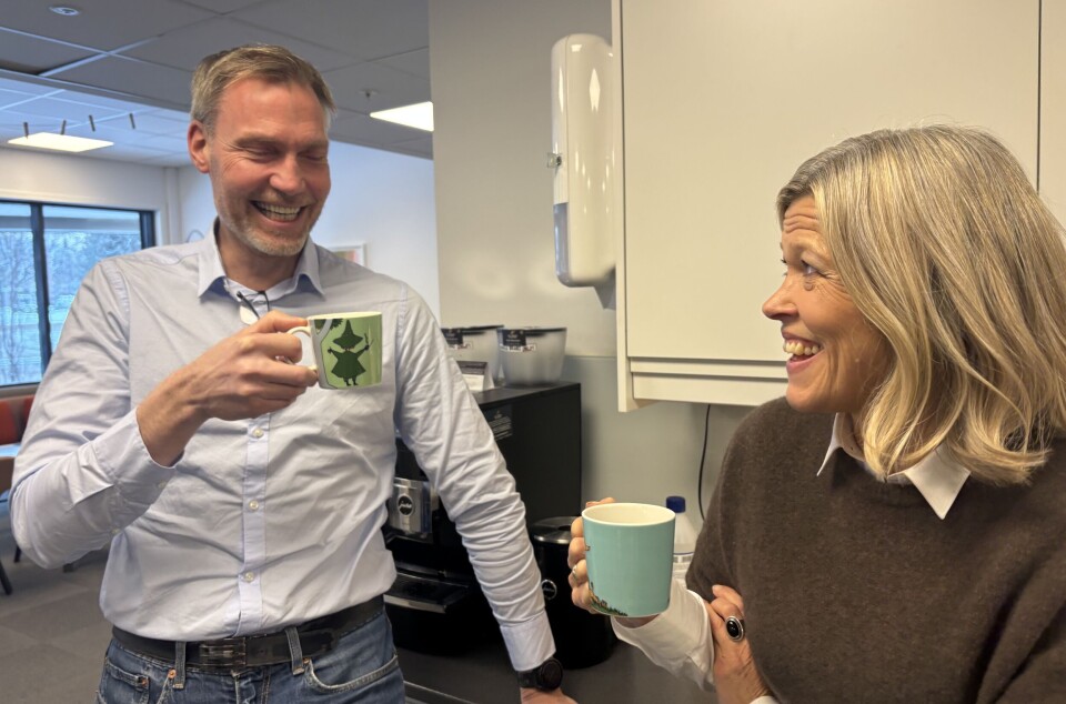 Smilende kvinne og mann med hver sin kaffekopp i hånda