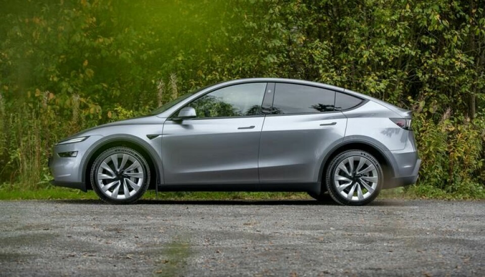 Sølv Tesla Model Y parkert på grusplass foran trær