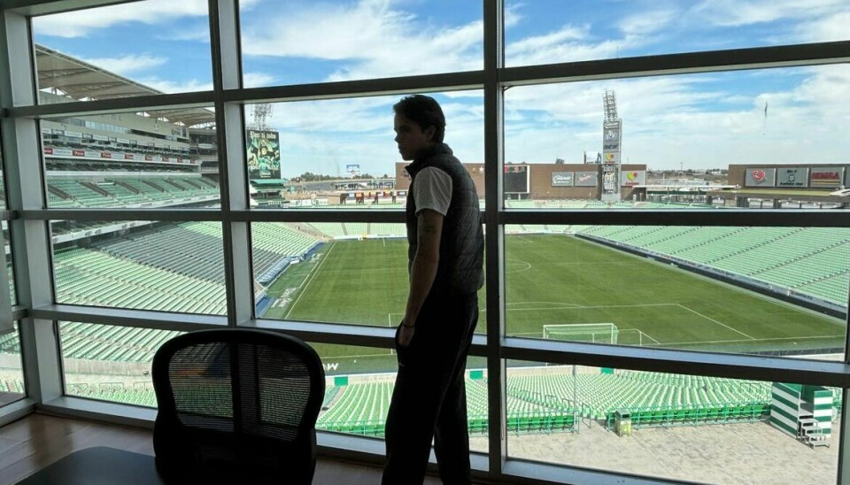 Person står ved panoramavindu og ser ut over en tom fotballstadion.
