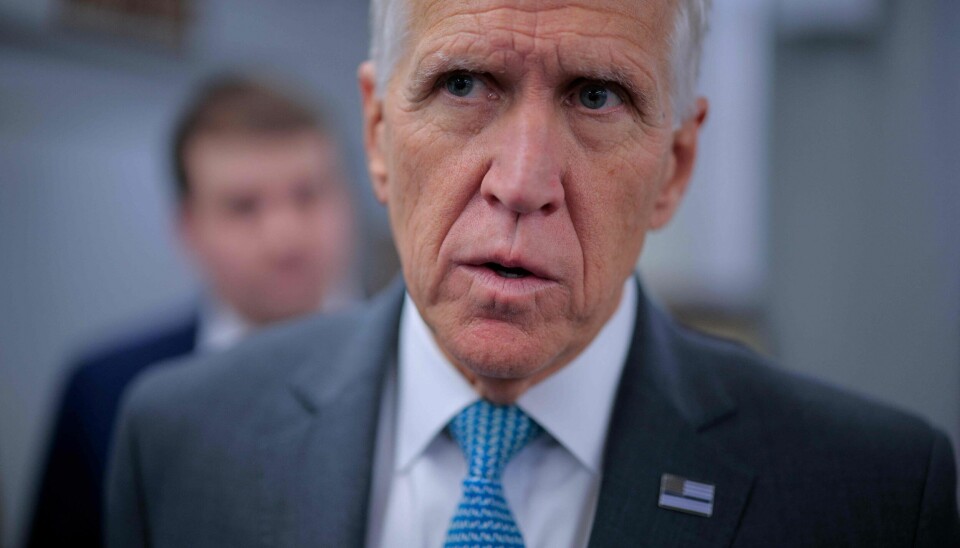 Nærbilde av mann i dress og blått slips innendørs med uskarp person i bakgrunnen