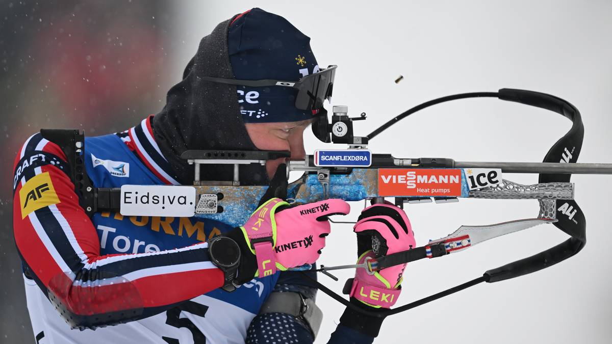 En skiskytter i teknisk utstyr sikter med riflen sin, klart fokusert på målet. Utøveren har på seg en jakke med nasjonsfarger og hansker i sterke farger. Snø faller lett i bakgrunnen, som gir kontekst til utendørsarrangementet. Nummeret "5" er synlig på utøverens rygg. (Bildebeskrivelsen er laget av en KI-tjeneste)