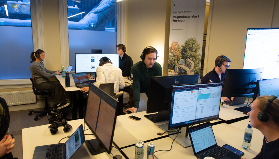 Unge ansatte med hodesett jobber ved skjermer i et åpent kontorlandskap.