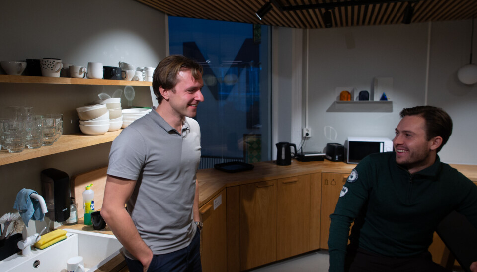 To personer står og sitter og snakker sammen på et moderne kontorkjøkken.