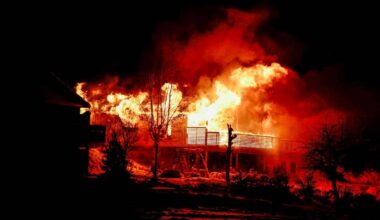 En bygning er i brann, med flammer som raser opp mot nattehimmelen. Omgivelsene er mørke, med trær og en annen bygning synlig i forgrunnen. Lysene fra flammene belyser området rundt. Det er ikke synlige personer i bildet. (Bildebeskrivelsen er laget av en KI-tjeneste)