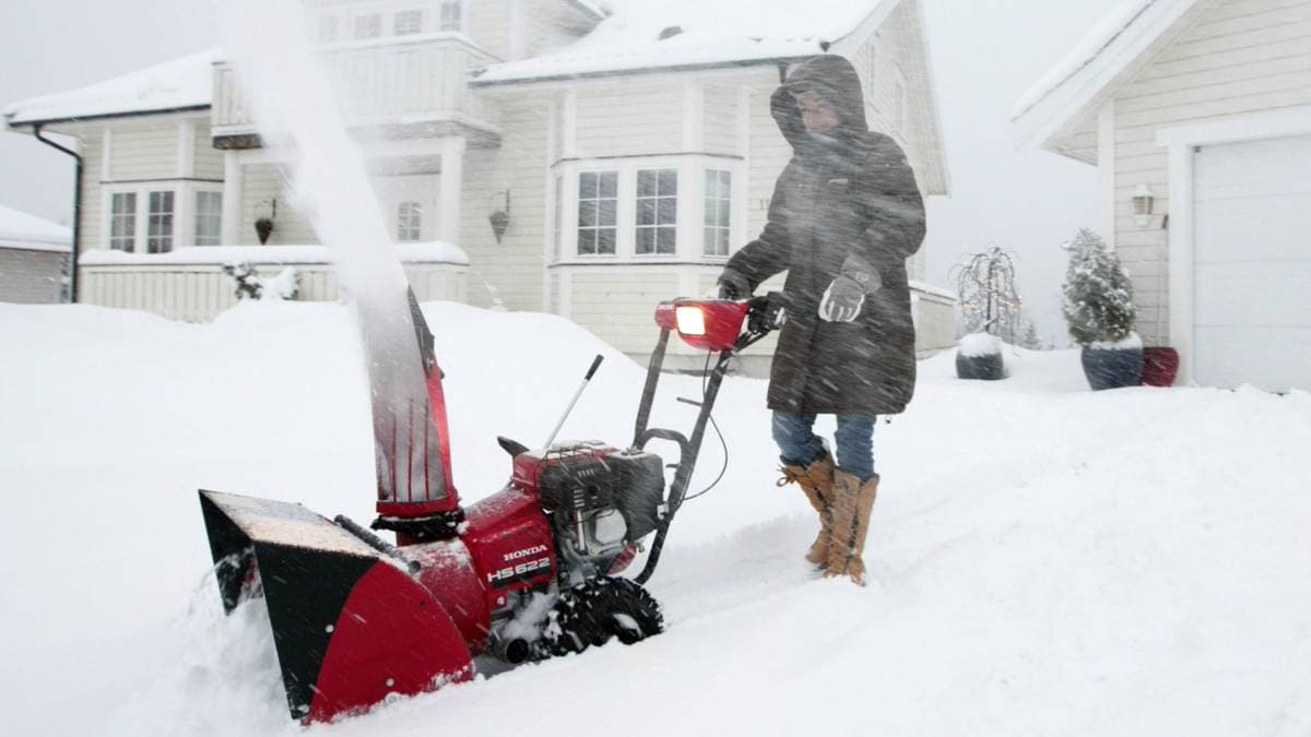 Kvinne som måker snø med snøfreser.